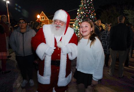 A person in a santa garment with a child in front of a christmas treeDescription automatically generated